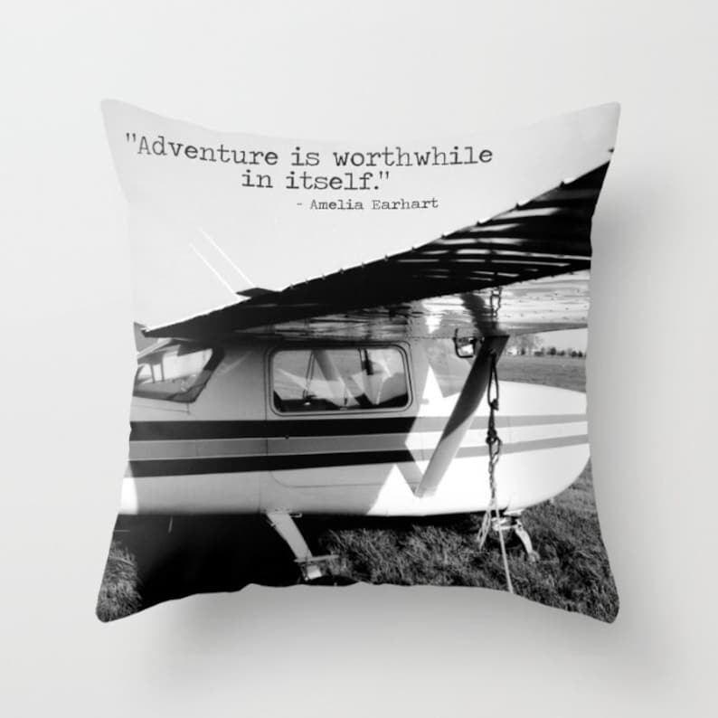 May include: Black and white photograph of a small airplane with the quote "Adventure is worthwhile in itself." - Amelia Earhart printed on top.
