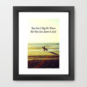 K&ouml;nnte beinhalten: Gerahmter Druck mit einer Strandszene und einer Person, die ein Surfbrett zum Meer tr&auml;gt. Der Text "You Can't Stop the Waves But You Can Learn to Surf" ist oben zu sehen. Das Bild hat eine warme, sonnige Farbpalette.