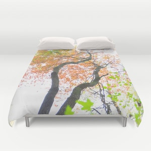 May include: A bed with a duvet cover featuring a tree canopy with orange and green leaves. The tree trunks are dark brown, and the background is a soft white. Two white pillows rest on the bed.