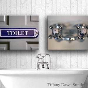 Pode incluir: Arte de parede de casa de banho com um letreiro azul e branco "TOILET" e puxadores de torneira cromados. Uma banheira branca está em primeiro plano. A imagem tem uma estética vintage.