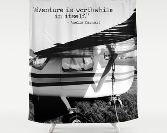 Peut inclure: Rideau de douche noir et blanc avec un avion vintage. Le rideau affiche une citation d'Amelia Earhart : "L'aventure vaut la peine en soi." L'avion a un corps blanc avec des rayures noires et grises et une hélice.