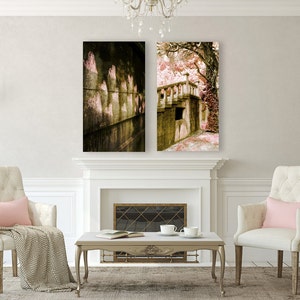 May include: Two framed landscape art prints above a fireplace. The left print shows a stone wall with arched openings, and the right print depicts a bridge with a staircase. The room features two armchairs, a coffee table, and a rug.