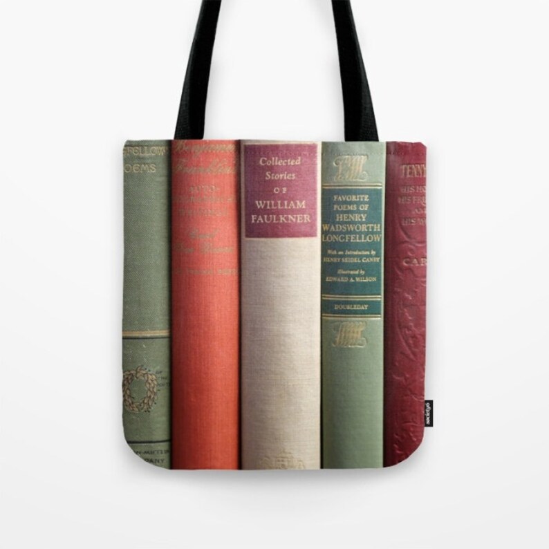 May include: Tote bag featuring a row of vintage book spines in various colors. The books include titles like "Collected Stories of William Faulkner" and "Favorite Poems of Henry Wadsworth Longfellow." The bag has black handles and a white background.