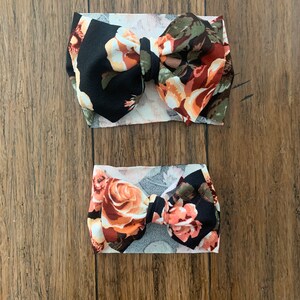 May include: Two floral print headbands with black and white fabric. The larger headband has a larger bow and the smaller headband has a smaller bow.