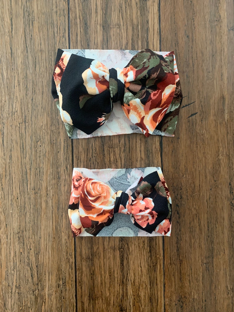 May include: Two floral print headbands with black and white fabric. The larger headband has a larger bow and the smaller headband has a smaller bow.