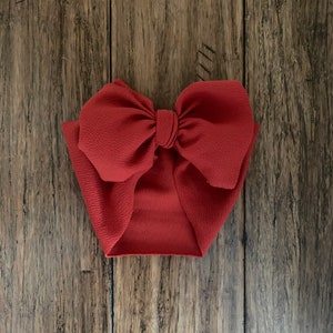 May include: A large, red fabric bow with a knotted center. The bow is made of a soft, textured material and is perfect for adding a touch of elegance to any outfit.