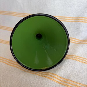 May include: A green funnel with a black rim. The funnel has a glossy finish and a small opening at the bottom. The object is set against a striped background.