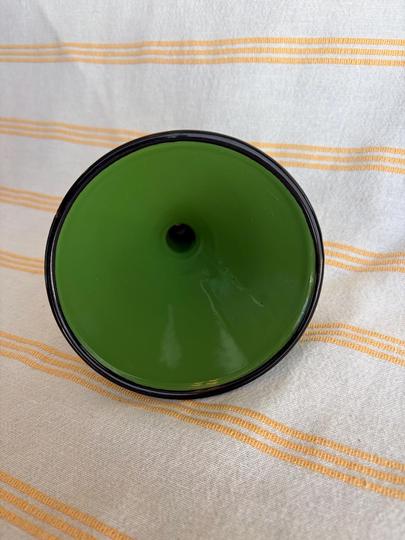 May include: A green funnel with a black rim. The funnel has a glossy finish and a small opening at the bottom. The object is set against a striped background.