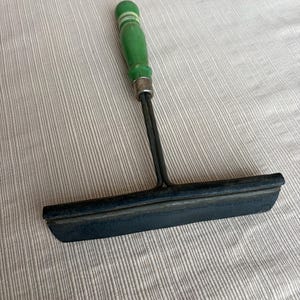 May include: A vintage window squeegee with a green wooden handle and a black rubber blade. The handle has white stripes and a metal ferrule. The squeegee is designed for cleaning windows and other smooth surfaces.