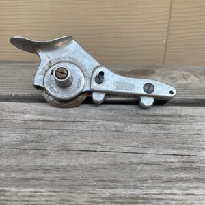 Puede incluir: Una herramienta de metal plateado con un mango y una rueda con el texto "The Mosty Trimmer Co.  Chicago, Ill. U.S.A."  La herramienta se utiliza para recortar tela.