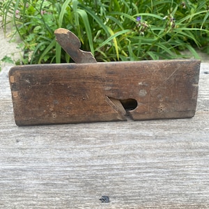 May include: A vintage wooden hand plane with a worn brown finish. The plane has a metal blade and a wooden handle.