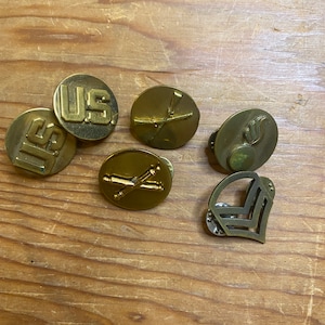 May include: Six gold-colored metal buttons with various designs. The buttons feature the letters "US", crossed rifles, a crossed cannon, a flame, and a chevron.