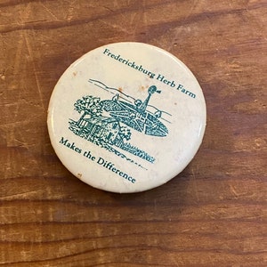 May include: A round, off-white button with the text "Fredericksburg Herb Farm" and "Makes the Difference" in green. The button features a green illustration of a building and a windmill.