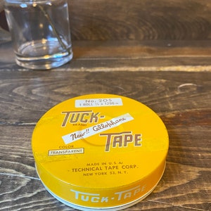 May include: A yellow round tin container with the text "Tuck-Tape" in a white circle on the lid. The text "New!! Cellophane Tape" is printed on the front of the tin. The text "No. 205 1 Roll 3/4 x 1296 in. Brand Color Transparent Made in U.S.A. Technical Tape Corp. New York 53, N.Y." is printed on the front of the tin.