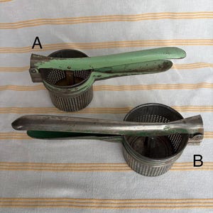 Puede incluir: Dos prensadores de patatas vintage con construcción metálica y mangos verdes. Los prensadores tienen un cuenco perforado y un mecanismo de palanca. El fondo es un paño blanco con rayas amarillas.