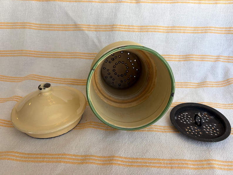 May include: A vintage, cream-colored ceramic coffee pot with a matching lid and a separate, perforated insert. The rim of the pot is accented with a green stripe. The pot is open, revealing the interior and the insert.