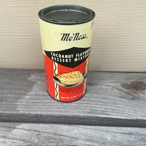 May include: A vintage metal can of MeNess Coconut Flavored Dessert Mix. The can is red, white, and black with a picture of a coconut cream pie on the front. The text on the can reads "MeNess Coconut Flavored Dessert Mix" and "Net Wt. 16 oz. (1 lb.)".