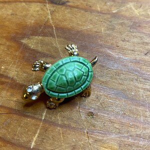 May include: A gold-colored turtle brooch with a green shell and rhinestones for eyes.