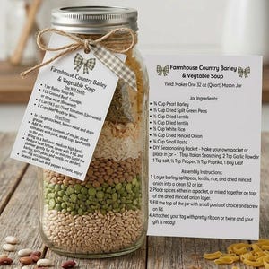 May include: A clear glass mason jar filled with layered dry soup ingredients including pearl barley, green peas, lentils, rice, and pasta. A twine bow and a white tag with the text Farmhouse Country Barley & Vegetable Soup are attached.