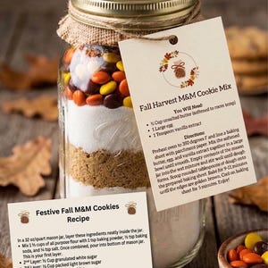 Peut inclure: Un bocal en verre de 1 litre rempli d'ingrédients pour biscuits en couches, incluant de la cassonade, du sucre blanc et des bonbons M&M aux couleurs d'automne. Le couvercle est recouvert de toile de jute et deux étiquettes en papier sont attachées.