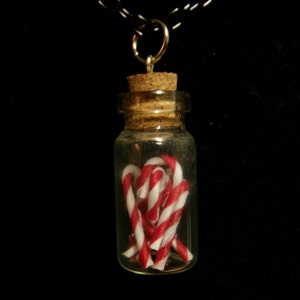 May include: A glass bottle necklace with a cork stopper filled with red and white candy canes.