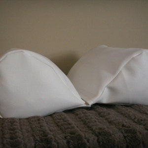 May include: Two white, fabric-covered pillows, shaped like a crescent moon, are placed together on a brown, fuzzy surface.