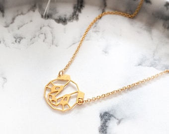 May include: A gold necklace with a geometric pendant shaped like a face. The necklace is on a white marble surface.
