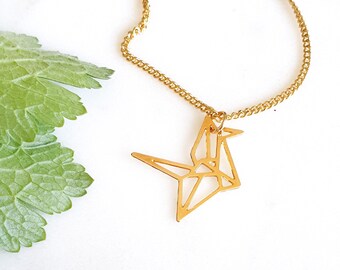 May include: A gold chain necklace with a delicate origami crane pendant. The pendant is made of thin metal and has a geometric design.