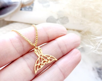 May include: A gold necklace with a delicate, geometric mermaid tail pendant. The pendant is made of a thin, openwork design and hangs from a delicate chain.