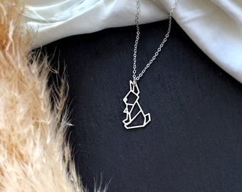 May include: A silver necklace with a geometric origami rabbit pendant. The necklace is on a white fabric background.