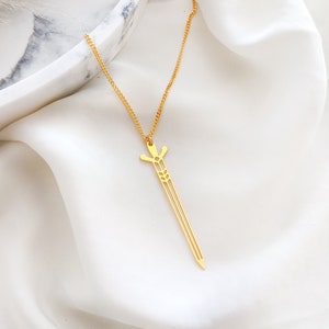 May include: A gold necklace with a sword pendant. The sword is a delicate, openwork design with a pointed tip.