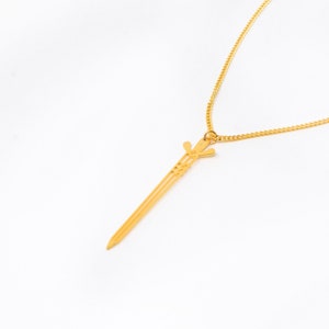 May include: A gold chain necklace with a sword pendant. The sword is detailed with intricate lines and a pointed tip.