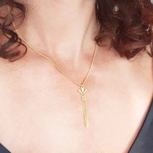 May include: A gold chain necklace with a sword pendant. The sword is a simple, geometric design.