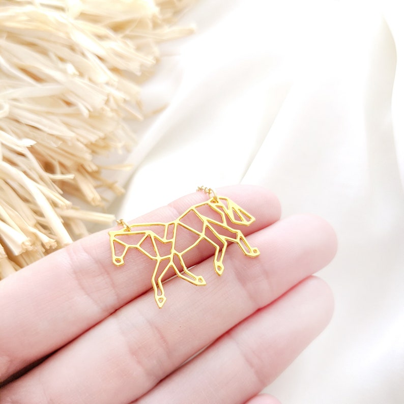 May include: A gold-toned necklace with a geometric horse pendant. The horse is made of thin metal and has a detailed, origami-like design.