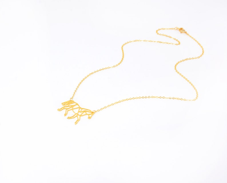 May include: A gold necklace featuring a geometric horse pendant. The chain is delicate and the pendant is detailed.