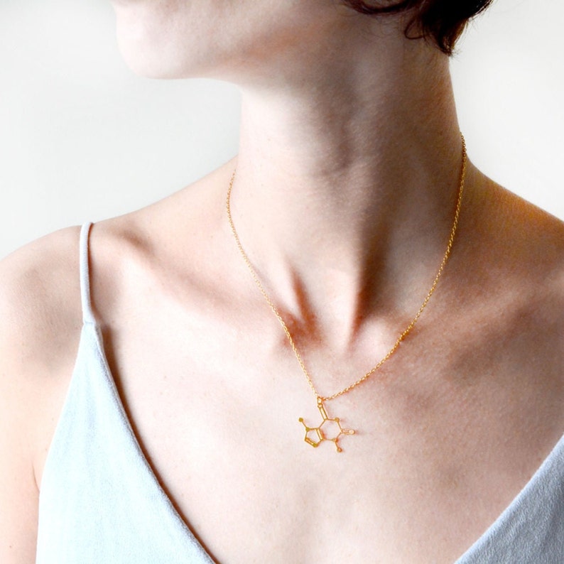 May include: A gold necklace with a pendant shaped like a chemical structure. The pendant is a stylized representation of a molecule.