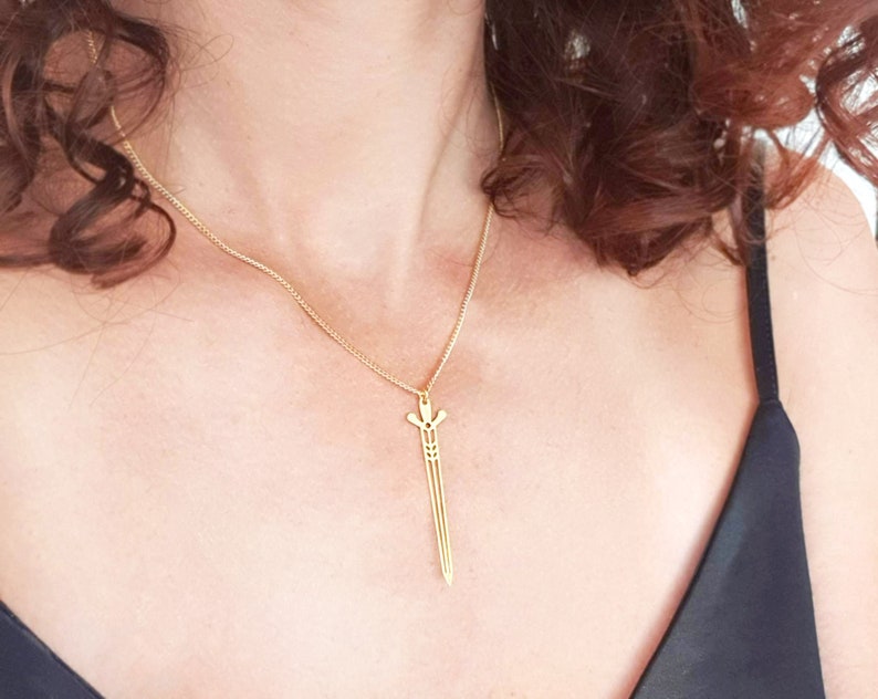 May include: A gold chain necklace with a sword pendant. The sword is a simple, geometric design.