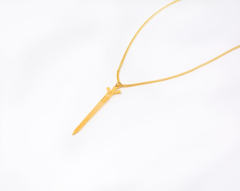 May include: A gold chain necklace with a sword pendant. The sword is detailed with intricate lines and a pointed tip.