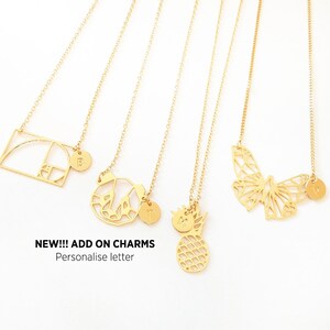 May include: Five gold necklaces with different charms, including a geometric shape, a butterfly, a pineapple, and two initial charms. The text "NEW!!! ADD ON CHARMS Personalise letter" is at the bottom of the image.