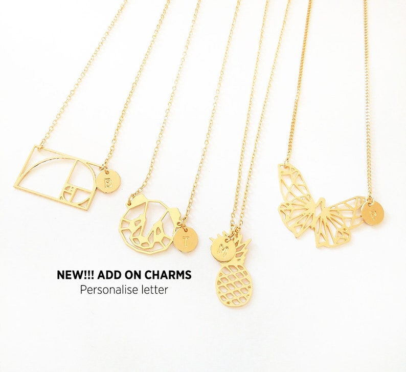 May include: Five gold necklaces with different charms, including a geometric shape, a butterfly, a pineapple, and two initial charms. The text "NEW!!! ADD ON CHARMS Personalise letter" is at the bottom of the image.