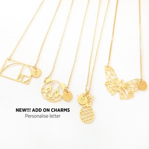 Puede incluir: Cinco collares de oro con diferentes colgantes, incluyendo una forma geom&eacute;trica, una mariposa, una pi&ntilde;a y dos colgantes con iniciales. El texto "NEW!!! ADD ON CHARMS Personalise letter" est&aacute; en la parte inferior de la imagen.