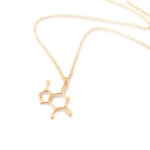 May include: A gold necklace with a pendant shaped like the chemical structure of dopamine. The necklace is made of a delicate chain.