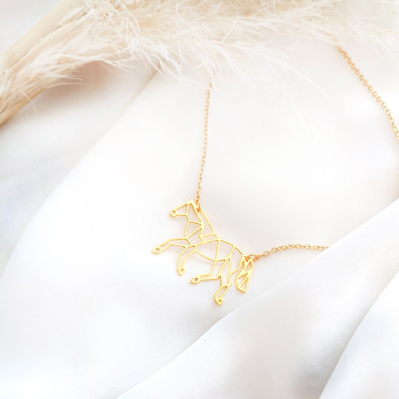 May include: A gold-toned necklace featuring a geometric horse pendant. The horse is crafted from thin metal and has a delicate, origami-like design.