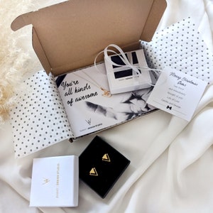May include: A white box with a black and white card inside that says "You're all kinds of awesome."  The box is open and there is a small white box with a gold necklace inside.  There is also a small white card with a black bow and the text "Merry Christmas Gems" and "Saw these and immediately thought of you! Lots of Love Camille and George".