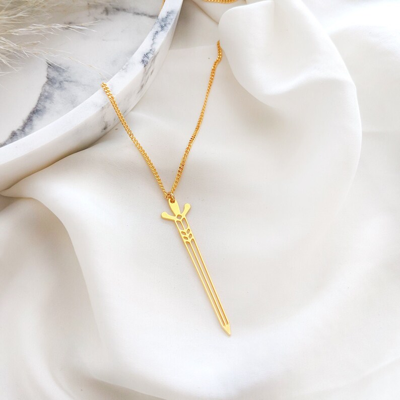May include: A gold necklace with a sword pendant. The sword is a delicate, openwork design with a pointed tip.