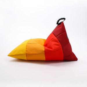 Könnte beinhalten: Ein bunter Sitzsack mit einem roten, orangen und gelben Patchwork-Muster. Der Sitzsack hat einen schwarzen Griff oben.