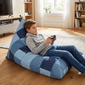 Puede incluir: Un puf azul grande con un diseño de retazos de varios tonos de azul. El puf está en un salón, lo que sugiere una opción de asiento informal y cómoda para relajarse o jugar.