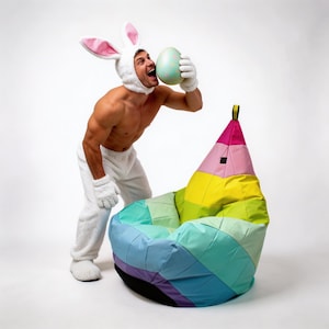 Könnte beinhalten: Ein bunter Sitzsack in Stiftform mit Regenbogenmuster. Der Sitzsack hat Paneele in Rosa, Gelb, Grün und Blau. Der Sitzsack befindet sich vor einem weißen Hintergrund.