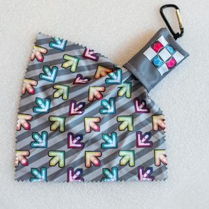May include: A gray microfiber cleaning cloth with a colorful arrow pattern. The cloth is folded and attached to a small gray pouch with a black carabiner clip.