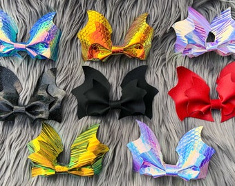 May include: A set of ten bat-shaped hair bows in various colors and patterns, including iridescent, red, black, and gold. The bows are made of fabric and have a center bow.